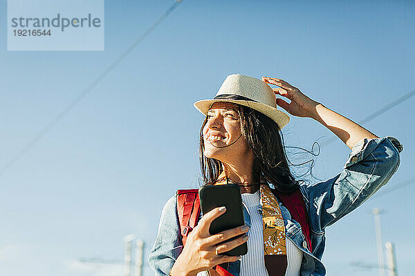 Glückliche Frau mit Hut und Smartphone unter dem Himmel