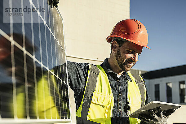 Lächelnder Ingenieur trägt schützende Arbeitskleidung und nutzt ein digitales Tablet mit Solarpanel