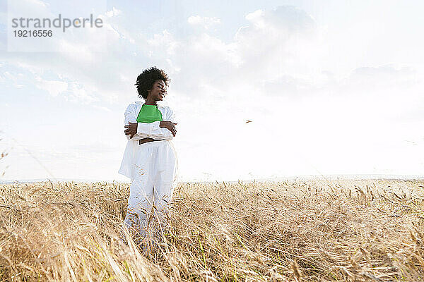 Carefree afro woman hugging self standing in field
