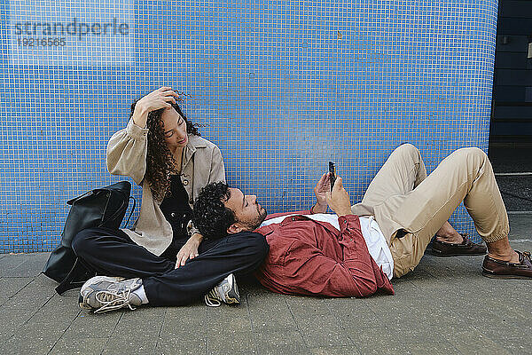 Junge Frau mit Mann entspannt sich und benutzt Smartphone in der Nähe der Wand