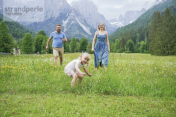 Happy daughter playing in meadow with father and mother on vacation