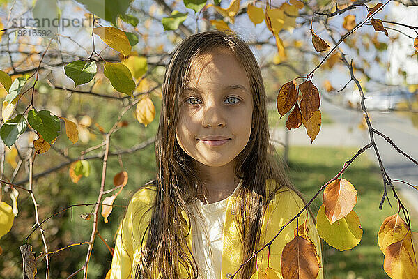 Lächelndes Mädchen  das inmitten von Blättern unter Zweigen steht