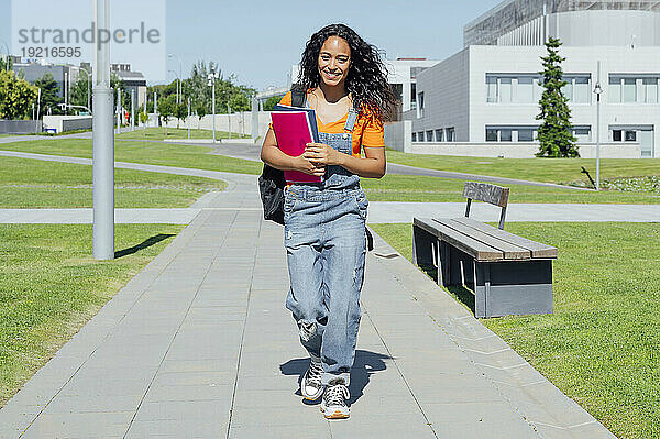 Fröhlicher Student hält Bücher in der Hand und geht auf dem Campus spazieren