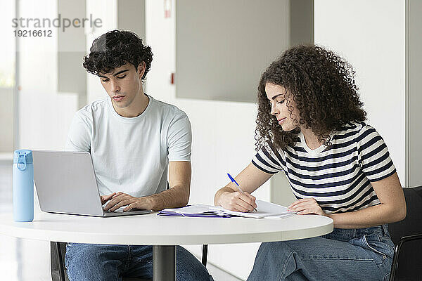 Junge Studenten schreiben an Büchern und benutzen Laptop am Tisch in der Universität