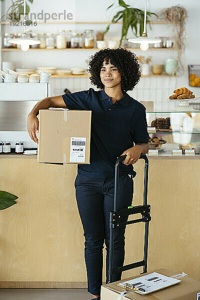 Delivery woman with curly hair standing with cardboard boxes in cafe