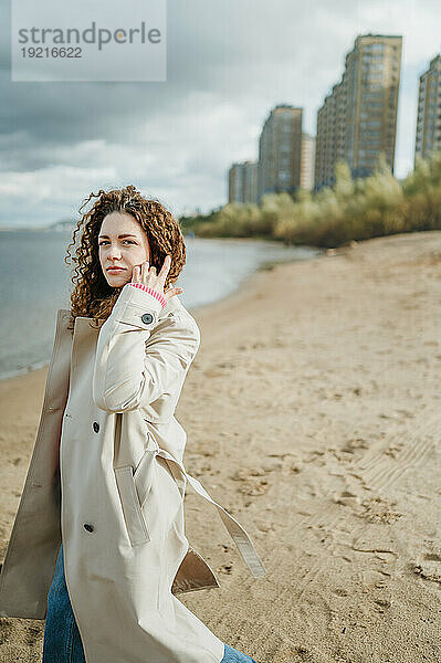 Frau im Trenchcoat steht auf Sand am Strand