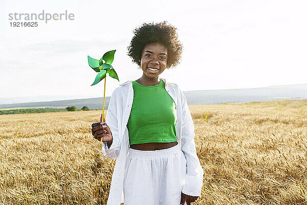 Young woman with afro hairstyle holding pinwheel toy standing in field