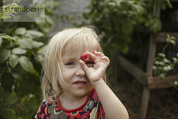 Playful girl holding raspberry in garden