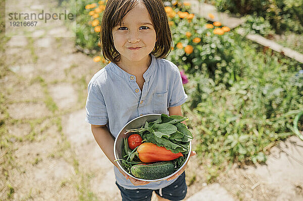 Smiling boy holding bowl of fresh organic vegetables