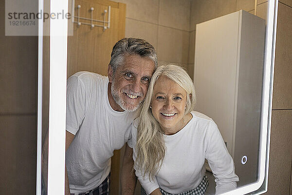 Spiegelbild eines glücklichen Mannes und einer glücklichen Frau im beleuchteten Spiegel zu Hause
