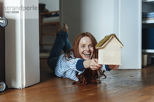 Happy redhead woman lying on floor with model house