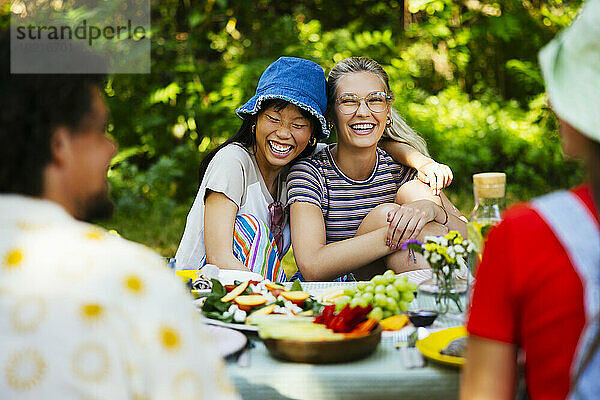 Fröhliche Freunde genießen das Essen am Picknicktisch im Garten