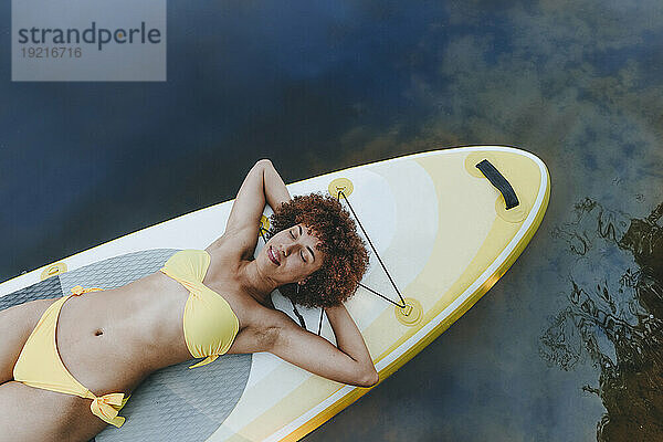 Lächelnde Frau liegt auf einem Paddleboard im See