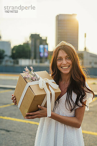 Glückliche Frau hält Geschenkbox bei Sonnenuntergang