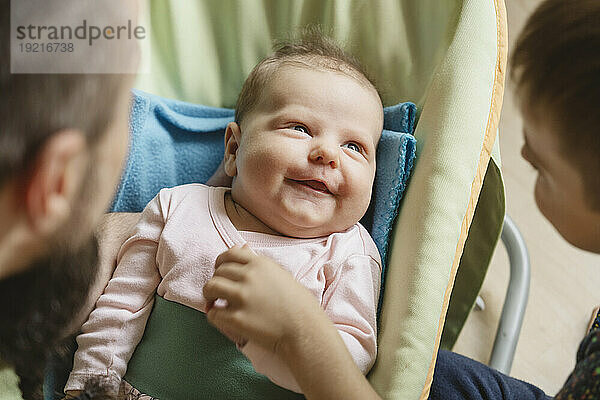 Smiling cute baby girl with father and brother at home