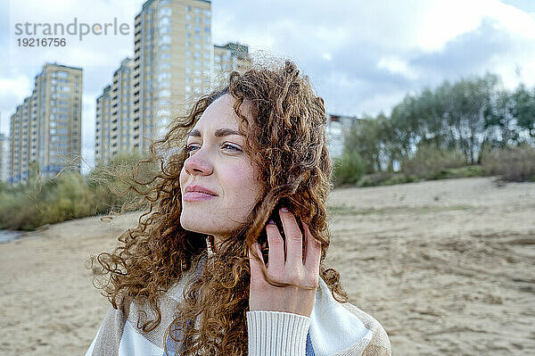 Schöne Frau mit lockigem Haar vor Gebäuden am Strand