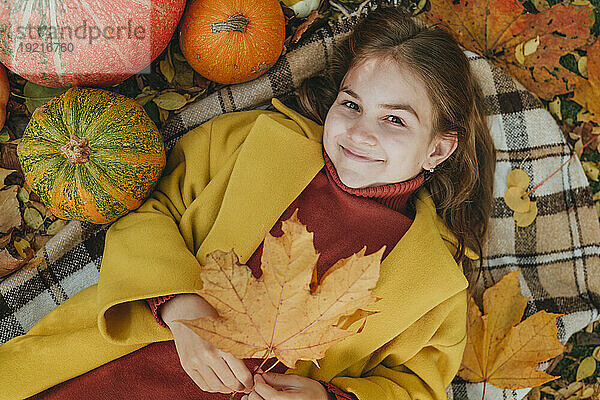 Smiling girl holding leaf and lying on blanket in garden
