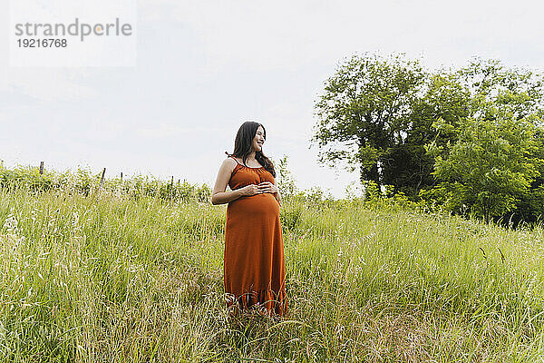 Schwangere Frau steht inmitten von Gras