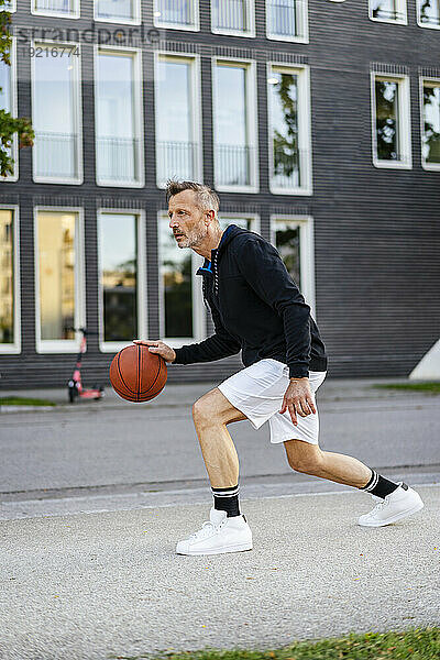 Reifer Athlet dribbelt Basketball auf dem Sportplatz