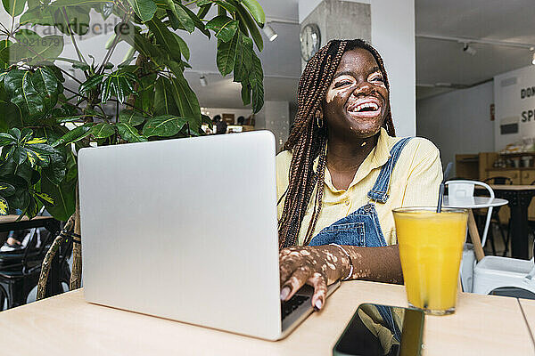 Glücklicher junger Freiberufler  der mit Laptop im Café sitzt
