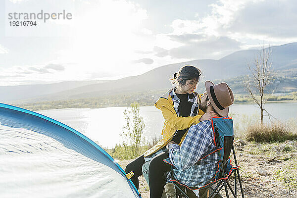 Freundin sitzt auf dem Schoß ihres Freundes am Zelt am See