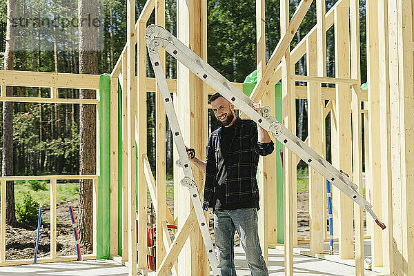 Lächelnder Ingenieur steht an einem sonnigen Tag neben einem Holzrahmen