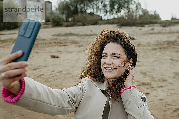 Lächelnde Frau macht Selfie mit Smartphone am Strand