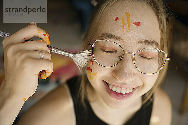 Happy woman painting face with paintbrush