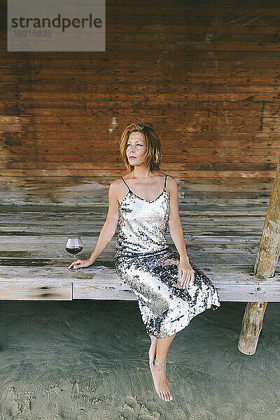 Thoughtful woman with wineglass sitting on wooden veranda
