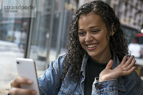 Glückliche junge Frau winkt bei einem Videoanruf über ihr Smartphone