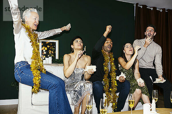 Fröhliche Familie mit mehreren Generationen jubelt auf dem Sofa  während sie zu Hause das neue Jahr feiert