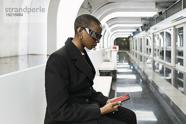 Junge Frau trägt eine intelligente Brille und benutzt ein Smartphone an der U-Bahn-Station