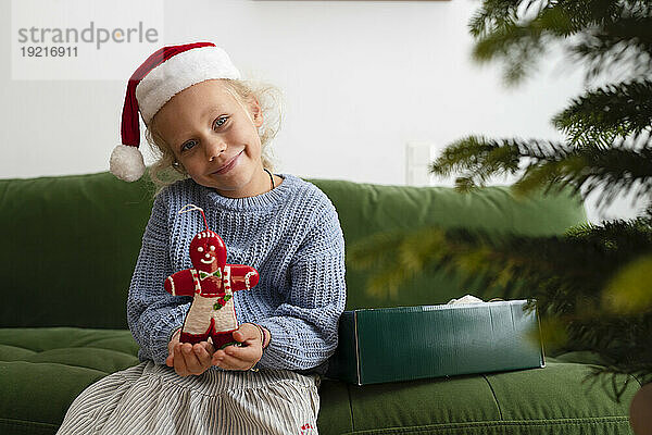 Lächelndes Mädchen hält Weihnachtsdekoration auf dem Sofa zu Hause