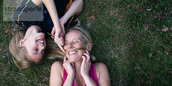 Smiling daughter touching mother's face and lying on grass in park