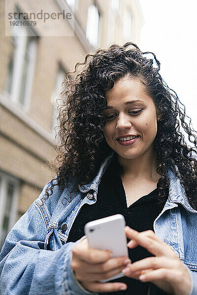 Lächelnde Frau mit lockigem Haar  die ihr Smartphone benutzt