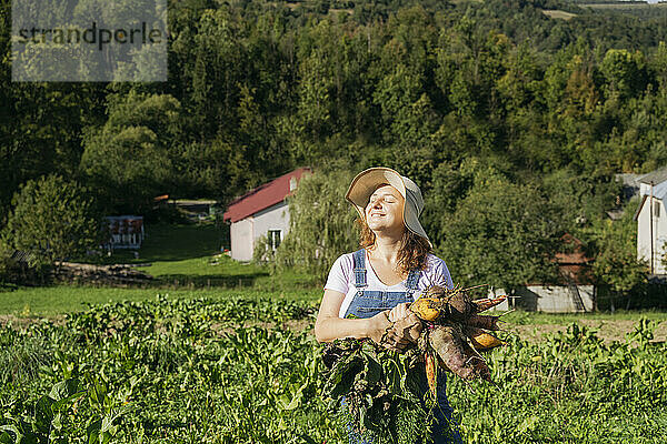 Frau mit Hut und Karotten im Feld an einem sonnigen Tag