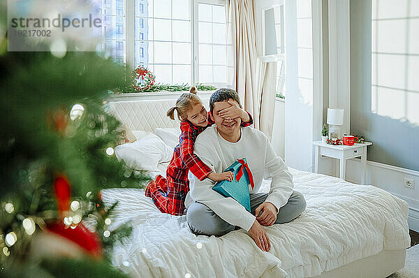 Tochter gibt Geschenk und bedeckt Vaters Augen zu Hause im Bett