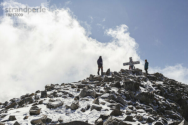 Freunde stehen in der Nähe des Gipfelkreuzes auf dem Berg