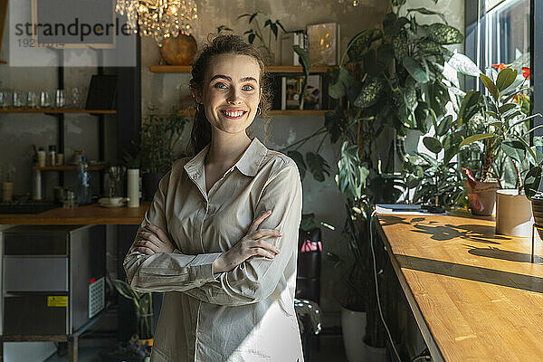 Glückliche Geschäftsfrau steht mit verschränkten Armen im Café