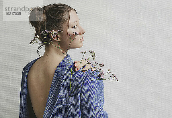 Teenage girl wearing blue blazer backwards with flowers in pocket by wall