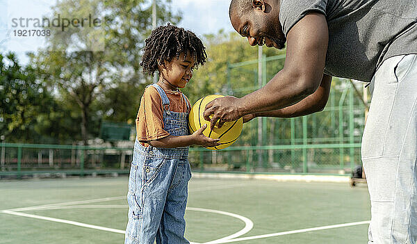 Lächelnder Vater gibt seinem Sohn Basketball auf dem Sportplatz