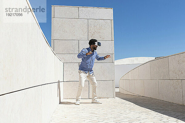 Mann beobachtet Virtual-Reality-Simulator  der an einem sonnigen Tag in der Nähe einer Wand steht