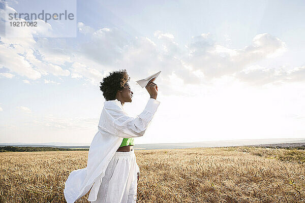 Carefree woman holding paper plane standing in field