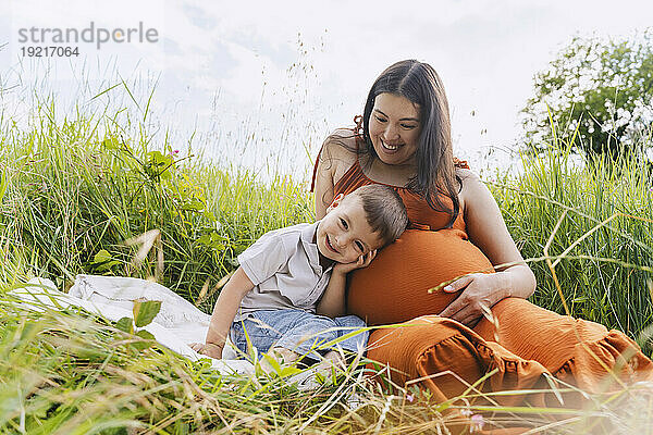 Happy pregnant mother and son spending leisure time in meadow