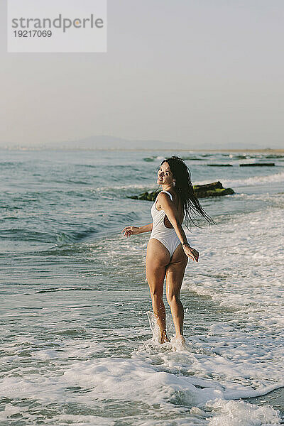 Lächelnde Frau läuft am Strand im Wasser