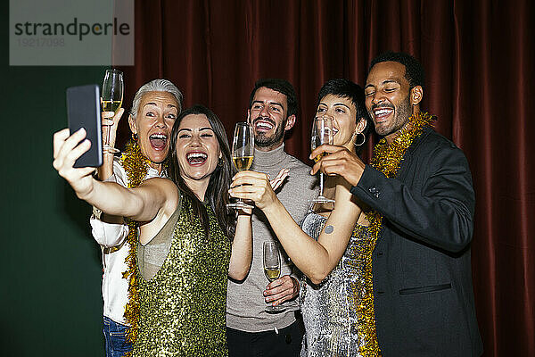 Familie mit Champagnergläsern macht Selfie mit dem Handy bei der Neujahrsparty zu Hause