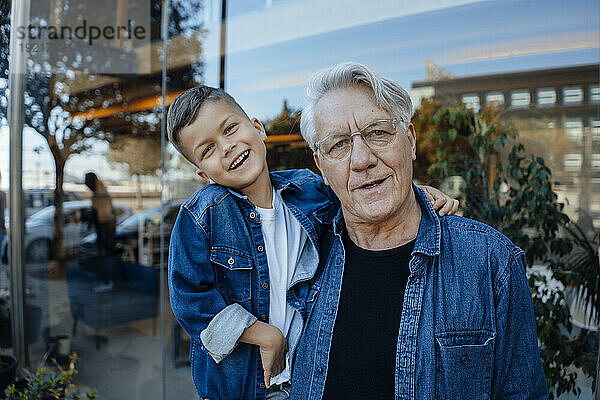 Happy boy with grandfather wearing denim shirt near wall