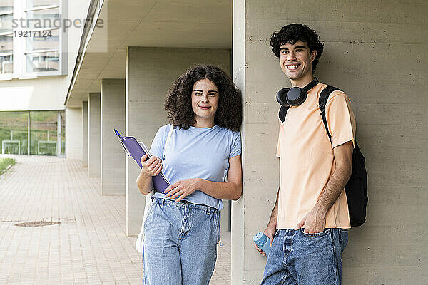 Lächelnde Studenten lehnen sich an die Wand auf dem Campus