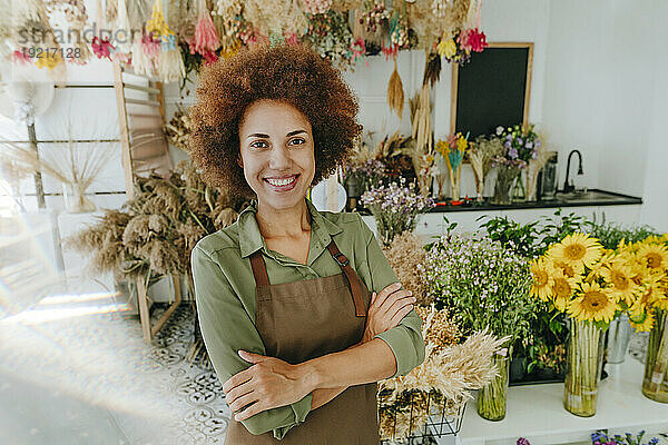 Lächelnder Florist mit verschränkten Armen im Blumenladen