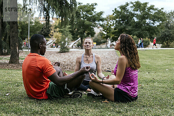 Multiethnische Freunde sitzen im Lotussitz und meditieren im Park